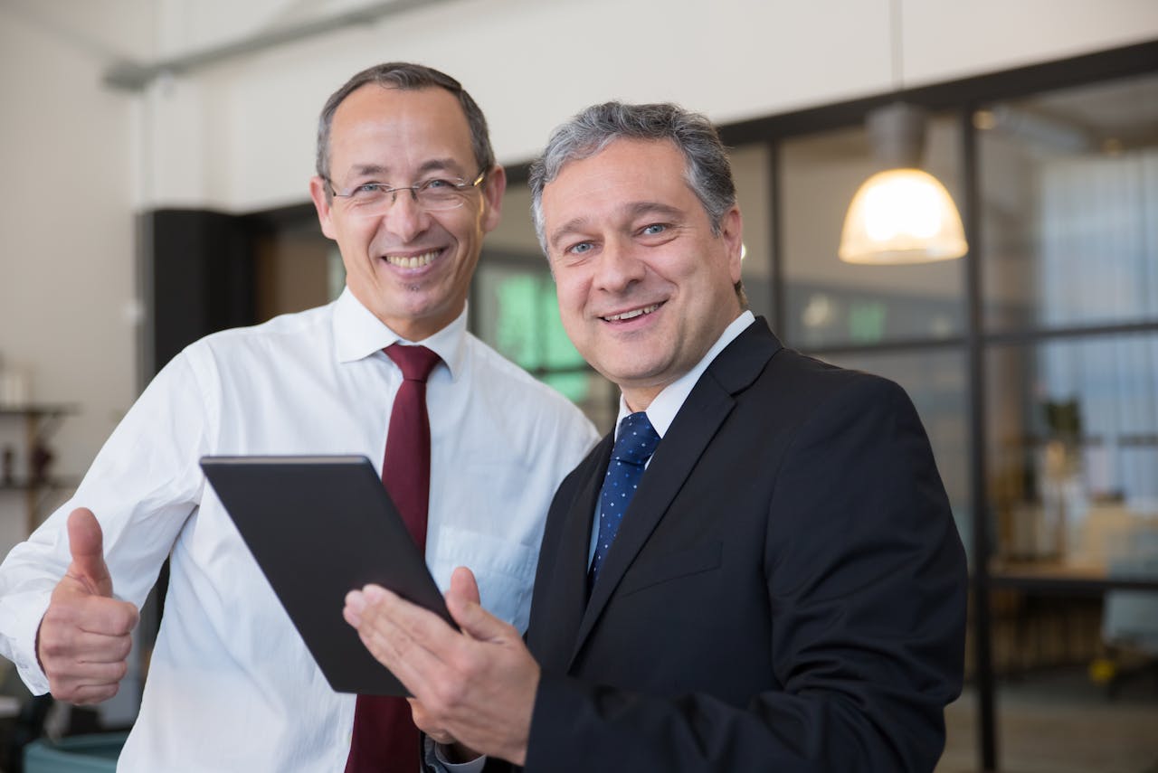 The Art of Drawing Readers In: Your attractive post title goes here Two smiling businessmen in corporate attire discussing work on a tablet in a modern office.